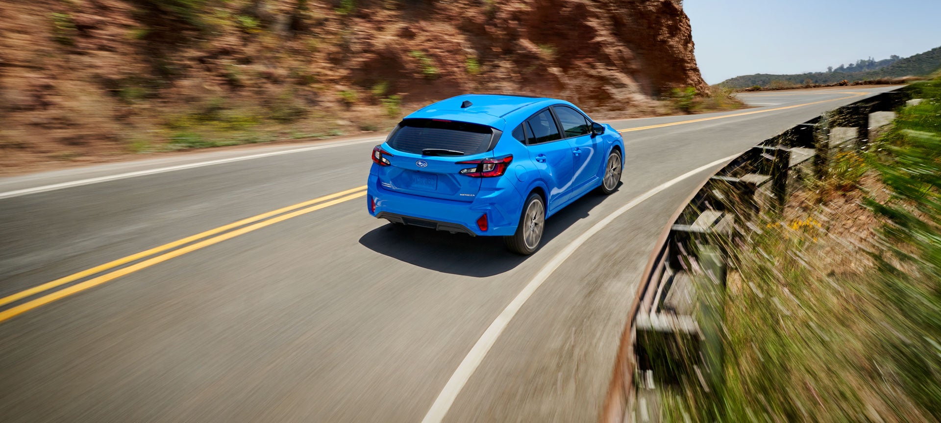 Blue 2024 Subaru vehicle driving uphill on curved mountain highway